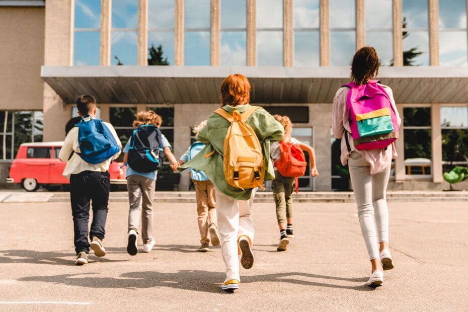 Kids running into school with backpacks on.