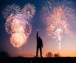 man holding sparkler in front of fireworks