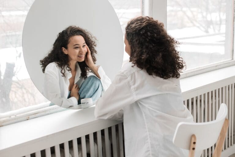 woman looking in mirror smiling symbolizing self love