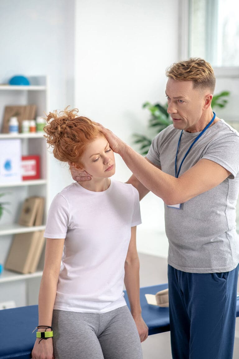 Male chiropractor examines patients neck in doctors office.