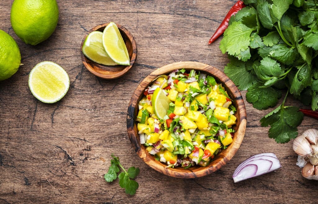 bowl of mango salsa with red onions, radishes, and cilantro rests on a table.